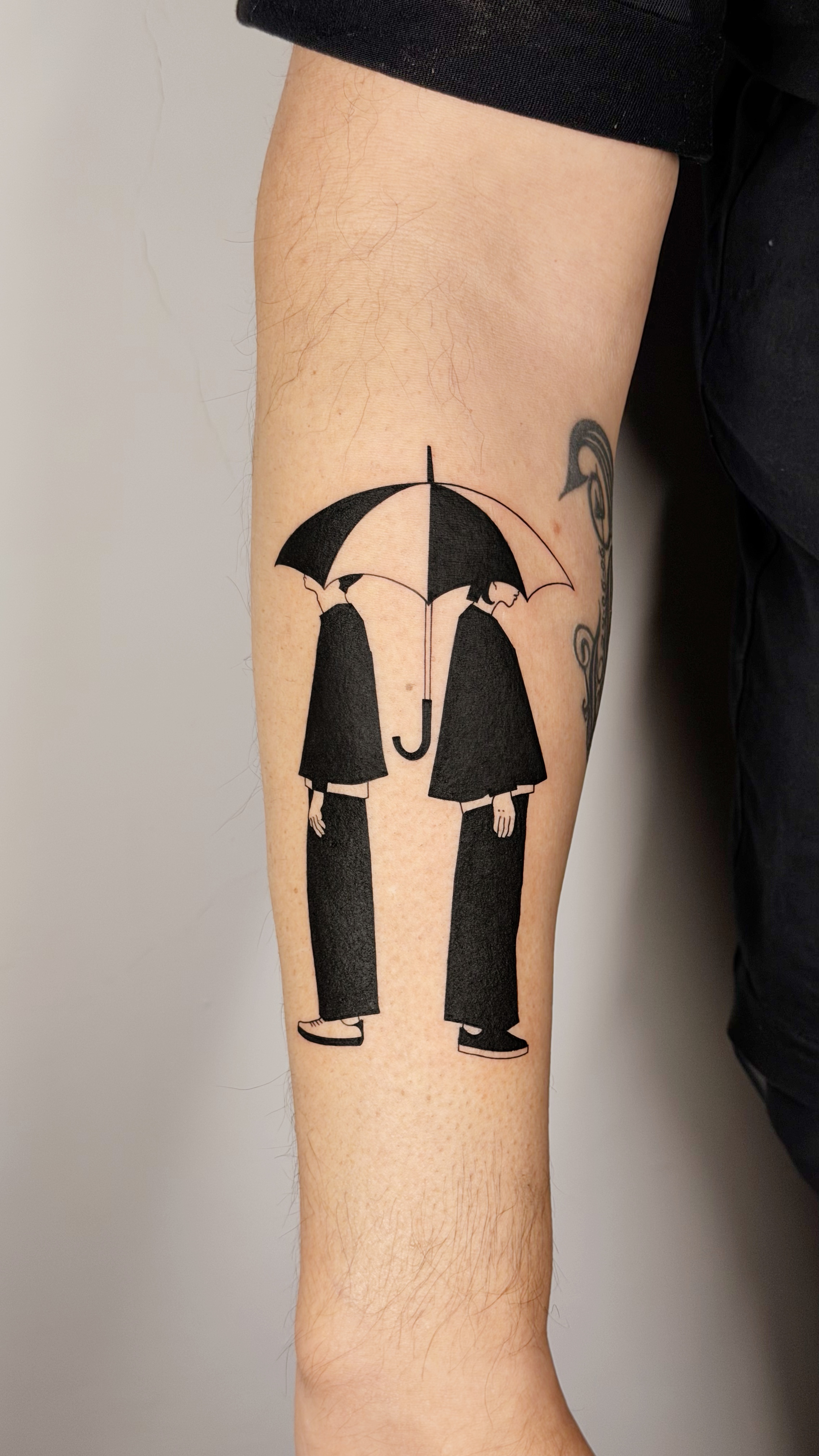 Blackwork tattoo of two figures sharing an umbrella in the rain on the arm — illustrative line work and graphic silhouette composition by Jane Again Tattoo, Mexico City.