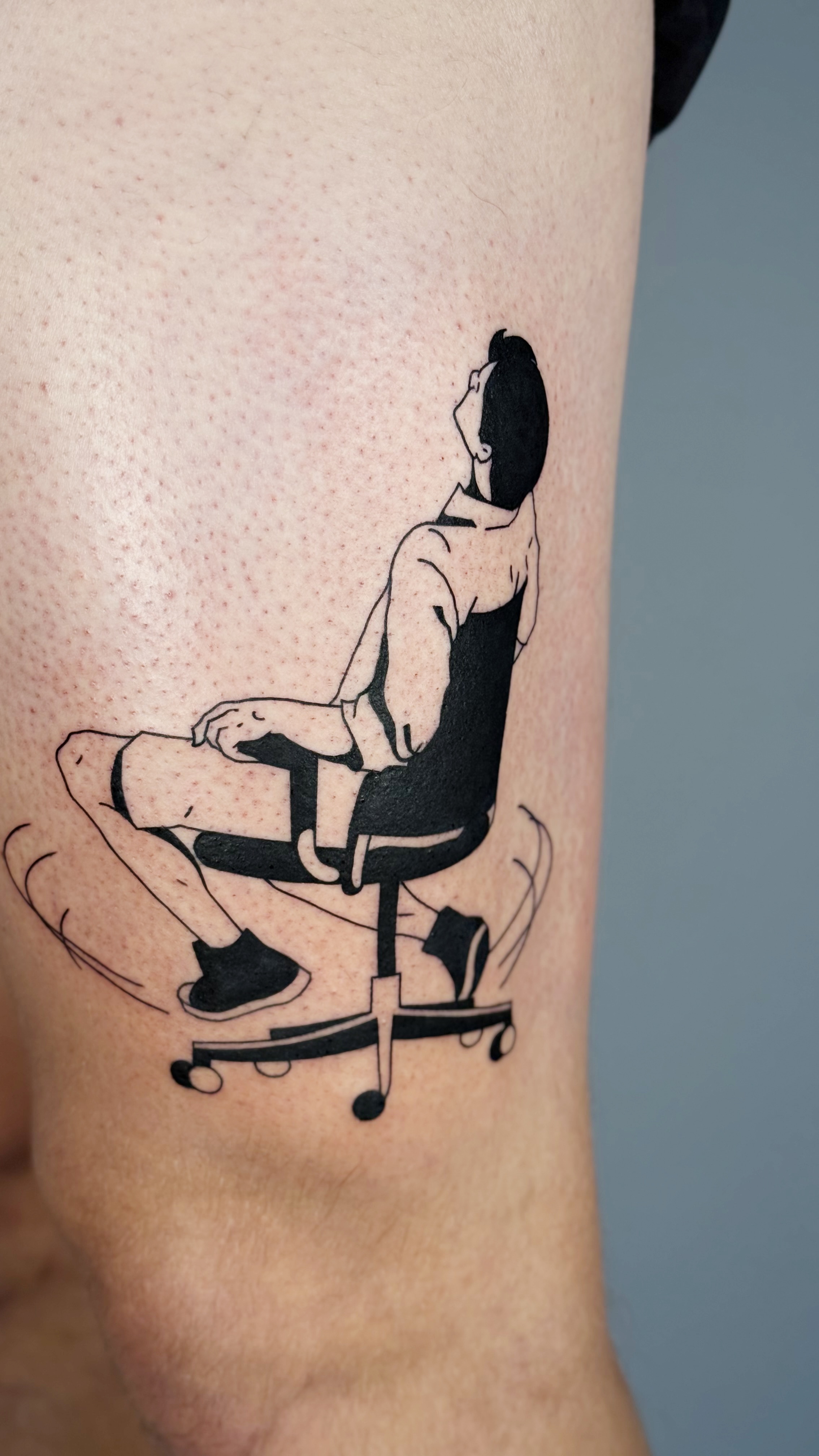 Blackwork thigh tattoo of a figure leaning back on an office chair — illustrative line work and graphic everyday-life narrative by Jane Again Tattoo, Mexico City.