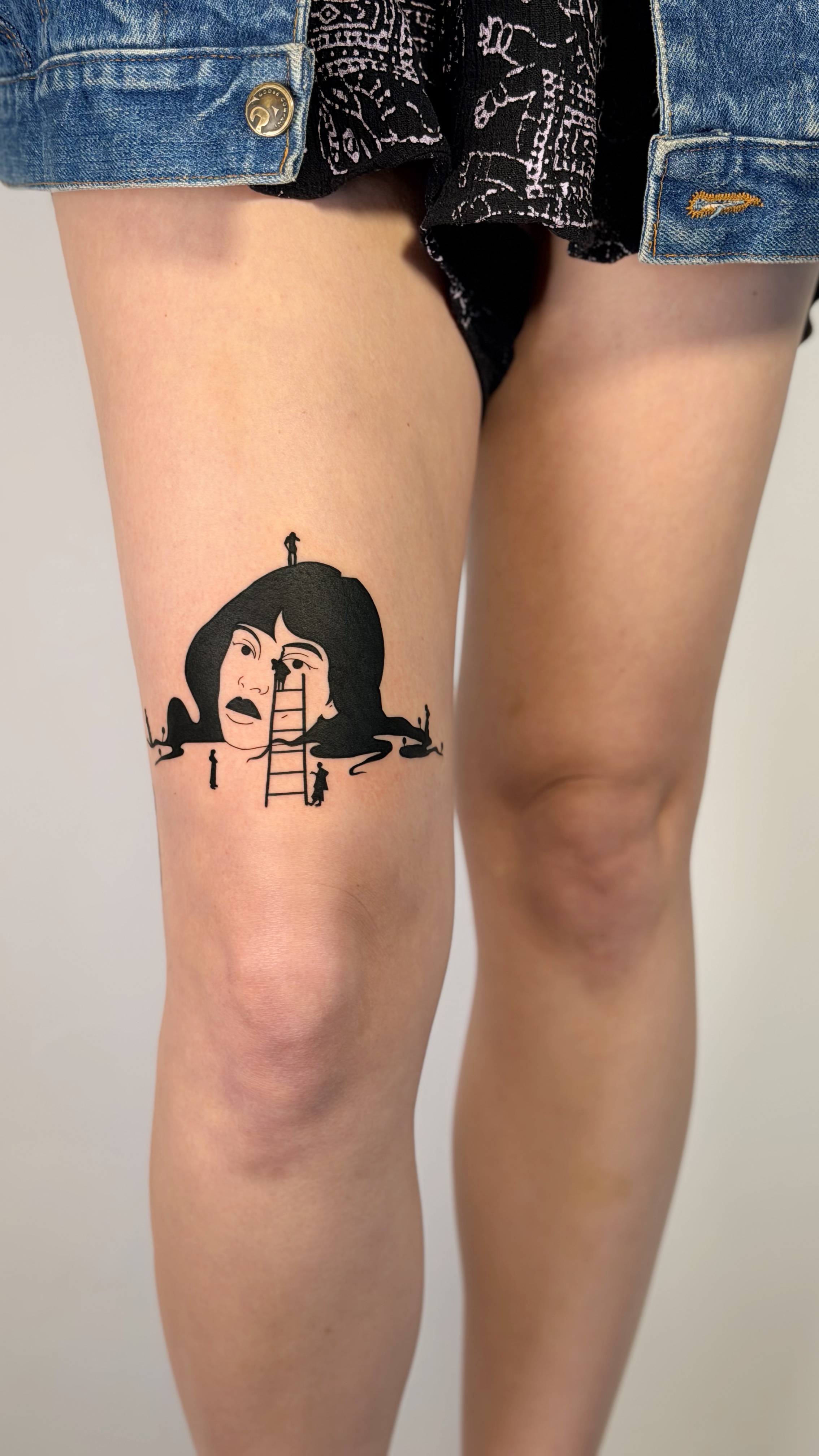 Blackwork knee tattoo of a stylized woman face with a ladder and small climbing figures — bold illustrative line work and graphic composition by Jane Again Tattoo, Mexico City.