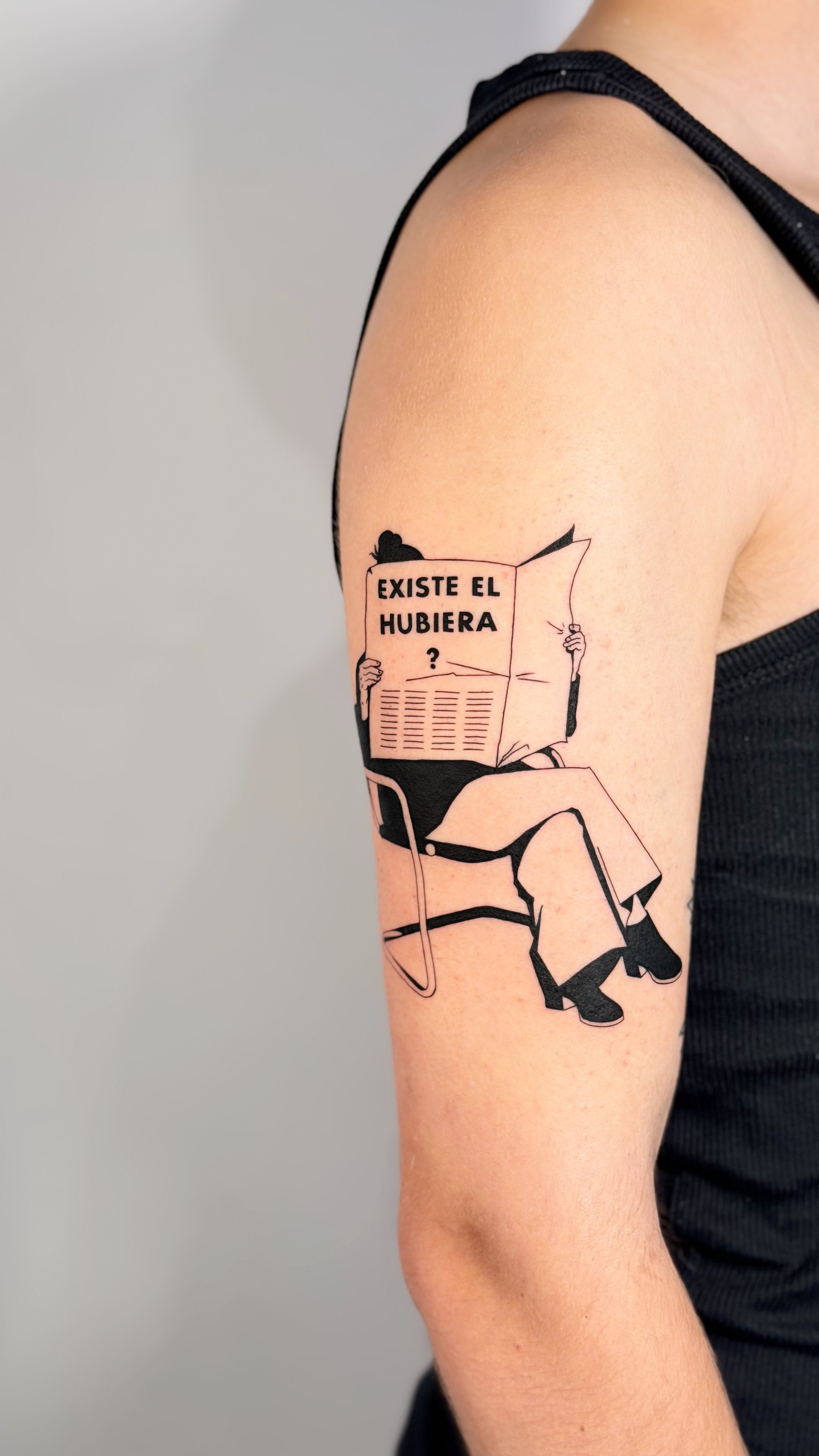 Blackwork arm tattoo of a person reading a newspaper titled 'Existe el Hubiera' — illustrative graphic line work and narrative composition by Jane Again Tattoo, Mexico City.