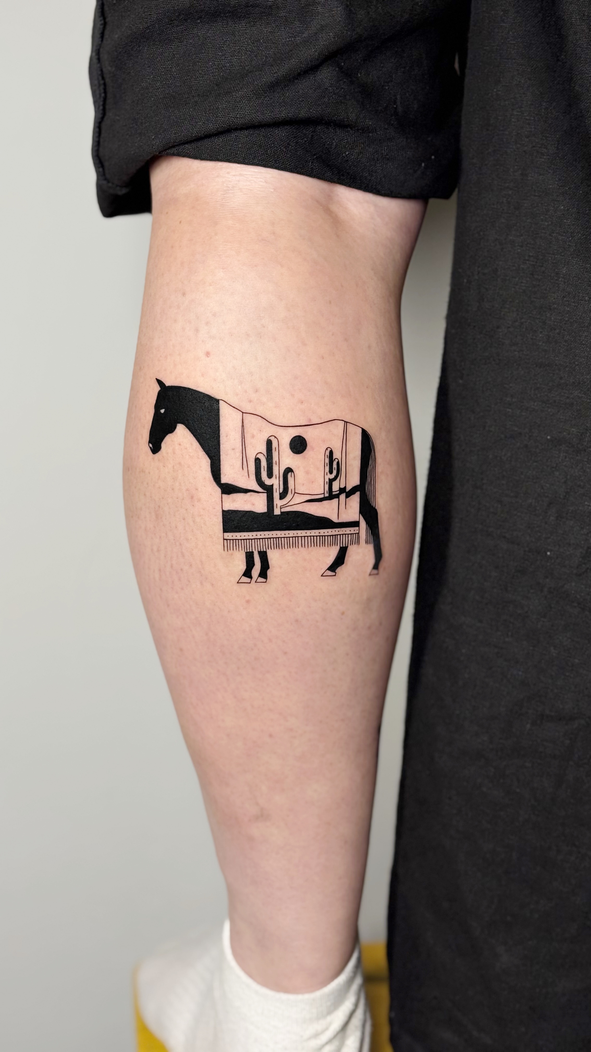 Blackwork calf tattoo of a horse silhouette with cactus and desert patterns on its body — bold graphic illustrative line work by Jane Again Tattoo, Mexico City.